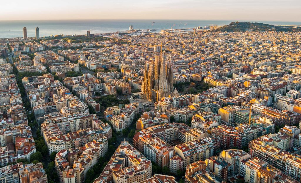 Aerial view of Barcelona, Spain, with the Sagrada Família basilica at the center and the coastline in the distance.