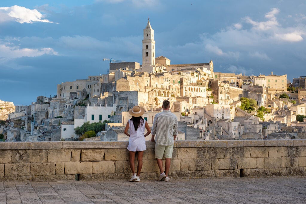Two people stand on a stone terrace, looking out over the historic hillside city of Matera, Italy.